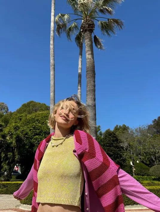 Foto terakhir memperlihatkan rambutnya yang tertiup angin menyapu wajahnya sementara dia mengenakan kemeja kuning, cardigan bergaris merah muda dan merah marun, serta kalung kerang berlapis. [@gigihadid]