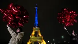 Para turis berpose dengan balon saat Menara Eiffel diterangi dengan warna-warna khas Ukraina untuk menandai peringatan satu tahun invasi Rusia ke negara tersebut, di Paris, Kamis, 23 Januari 2023. Pada 24 Februari 2022 lalu Rusia menginvasi Ukraina dan menandai puncak eskalasi konflik kedua negara sejak 2014 silam. (AP Photo/Christophe Ena)