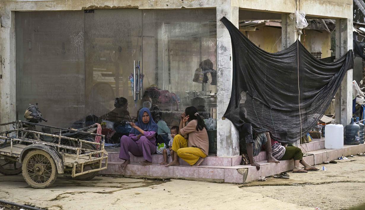 Penyakit ini disebabkan oleh kontak korban banjir yang terkontaminasi oleh kuman berbahaya. Tampak dalam foto, sebuah keluarga menggunakan toko kosong sebagai tempat berlindung setelah banjir bandang melanda daerah tersebut di Aceh Tamiang, Provinsi Aceh, pada Sabtu 6 Desember 2025. (YT HARIONO/AFP)