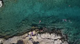Orang-orang berenang di laut di pinggiran Vouliagmeni, barat daya Athena, Yunani, Kamis (29/7/2021). Gelombang panas membuat orang-orang berbondong-bondong ke pantai, air mancur umum, dan lokasi ber-AC. (AP Photo/Yorgos Karahalis)