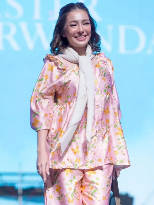 Maya Septha juga mengenakan setelan baju tidur warna pink dengan atasan lengan 3/4 dipadukan celana panjang. Ia juga mengenakan syal putih dan membawa tas coklat. [@sarwendah29]