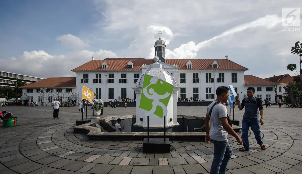 Pengunjung melintas dekat ornamen Asian Games 2018 di kawasan Kota Tua, Jakarta, Senin (4/12). Ornamen tersebut untuk mengajak warga mensukseskan dan memeriahkan acara yang akan berlangsung pada 18 Agustus-2 September. (Liputan6.com/Faizal Fanani)
