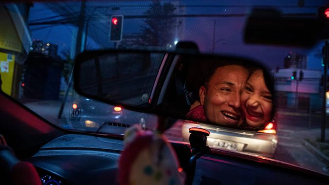 Jose Collantes mendapat pelukan dari sang putri, Kehity saat berhenti di lampu merah, tiga bulan setelah kematian istrinya akibat COVID-19 di Santiago, Chili, 6 September 2020. Mereka yang selamat dari pandemi dan yang kehilangan orang yang dicintai, hidupnya tidak pernah sama. (AP/Esteban Felix)