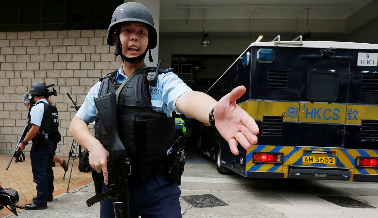 Polisi bersenjata lengkap menjaga ketat saat mobil yang membawa Rurik Jutting ke Pengadilan Tinggi di Hong Kong, Tiongkok (24/10). Jutting mengaku menyiksa korbannya selama tiga hari dan merekam aksinya. (Reuters/Bobby Yip)