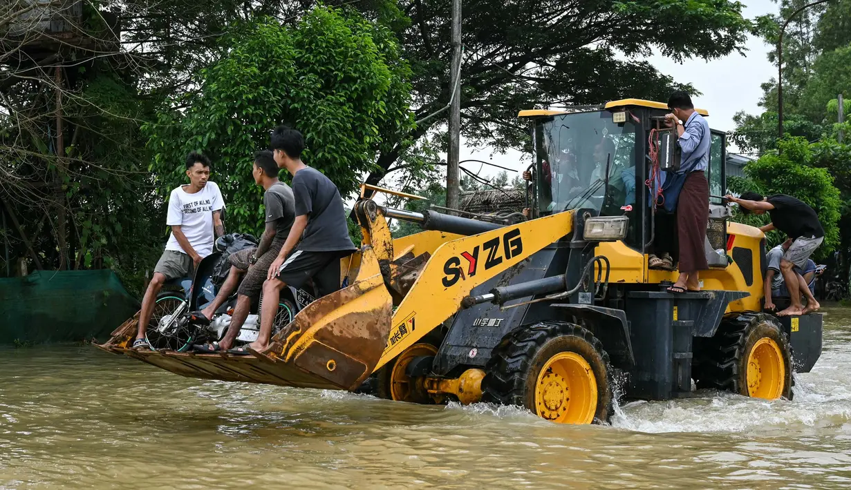 Orang-orang mengendarai buldoser melewati jalan yang tergenang banjir di kota Hpa Yar Gyi di wilayah Bago, Myanmar, pada tanggal 9 Oktober 2023. (SAI AUNG MAIN/AFP)