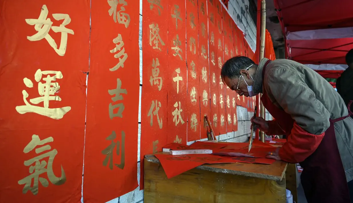 Seorang kaligrafer menulis kuplet musim semi, semacam dekorasi Tahun Baru Imlek, jelang dimulainya Tahun Baru Imlek di sebuah kios di Foshan, Provinsi Guangdong, China, 18 Januari. Kuplet biasanya dipasang melintang di kusen pintu. (Giok Gao/AFP)