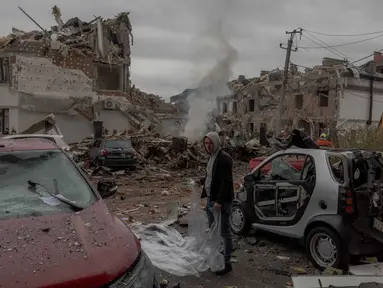 Seorang pria bersiap menutupi mobil yang rusak dengan lembaran plastik di lokasi bangunan tempat tinggal yang rusak parah akibat serangan udara Rusia di pinggiran kota Kyiv, pada 28 September 2025, di tengah invasi Rusia ke Ukraina. (Roman PILIPEY/AFP)