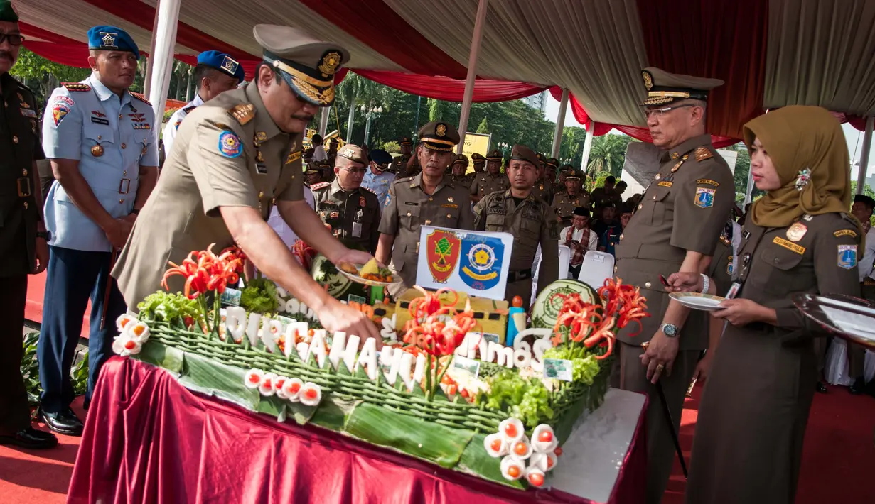 Djarot Saiful Hidayat memotong tumpeng saat upacara hari ulang tahun Satpol PP dan Satuan Perlindungan Masyarakat (Satlinmas) di Jakarta, Kamis (27/4). (Liputan6.com/Gempur M. Surya)