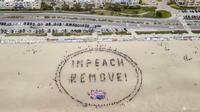 Para pengunjuk rasa membentuk spanduk manusia bertuliskan "Impeach and Remove" di Ocean Beach selama protes terhadap Presiden AS Donald Trump, di San Francisco, 19 April 2025. (San Francisco Chronicle via AP/Stephen Lam)