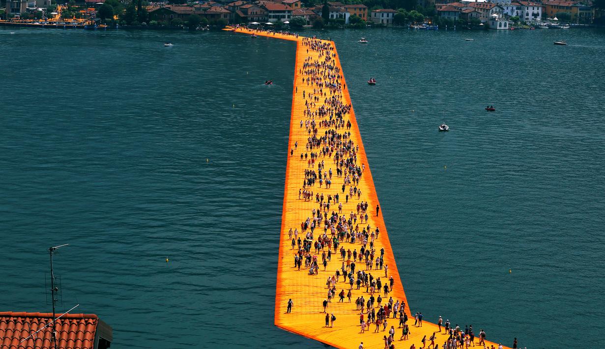 Ribuan wisatawan berjalan di atas instalasi "The Floating Piers" di Danau Iseo, Italia utara, (24/6). Seni instalasi sepanjang 1,9 mil ini terbuat dari 200.000 batu apung yang ditutupi kain oranye. (REUTERS/Stefano Rellandini)