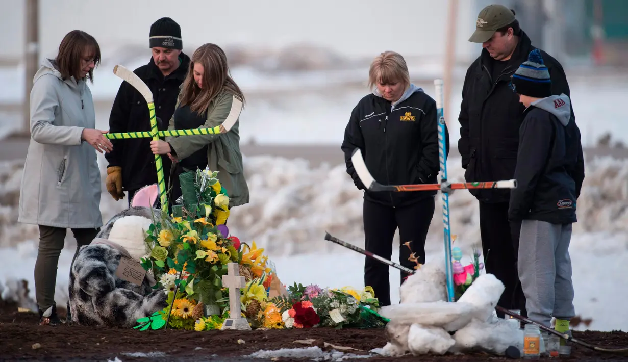 Sebuah keluarga menempatkan salib yang terbuat dari tongkat hoki untuk memberi penghormatan kepada korban kecelakaan bus yang membawa tim hoki es Humboldt Broncos di Provinsi Saskatchewan, Kanada (9/4). (Jonathan Hayward/The Canadian Press via AP)