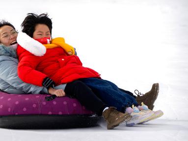 Seorang wanita dan seorang anak yang mengenakan masker meluncur menuruni bukit tertutup salju dengan ban dalam di taman umum saat pekan liburan Tahun Baru Imlek di Beijing, China, Kamis (26/1/2023). (AP Photo/Mark Schiefelbein)