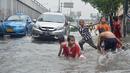 Anak-anak asyik bermain genangan air di Jalan Pramuka, Jakarta, Minggu (1/2/2015). (Liputan6.com/Andrian M Tunay)