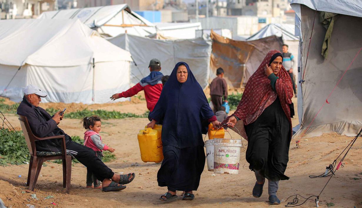 Kondisi ini memaksa jutaan warga Palestina di Gaza mengantre berjam-jam setiap kali truk bantuan air bersih datang, dengan jatah yang terkadang hanya tersedia seminggu sekali. Tampak dalam foto, para wanita berjalan membawa ember air dan jerigen setelah mengisi air dari tangki portabel di kamp pengungsi Palestina Maghazi, Jalur Gaza tengah pada Rabu 11 Februari 2026. (Eyad BABA/AFP)