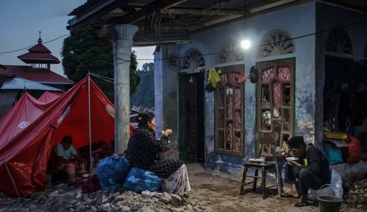 Keluarga korban banjir bandang berbuka puasa Ramadan di tempat penampungan sementara berlatar rumah yang hancur di Ganting, Sumatera Barat pada 14 Maret 2024. (REZAN SOLEH/AFP)
