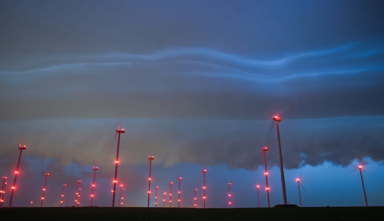 Badai awan gelap terlihat di langit di atas turbin angin di Sieversdorf, Jerman (10/6/2019). (AFP Photo/dpa/Germany Out/Patrick Pleul)