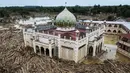 Jejak bekas lumpur dan air banjir pun masih terlihat di dinding dekat atap lantai dua bangunan. Tampak foto udara menunjukkan tumpukan pohon tumbang yang tersapu banjir bandang sekitar tiga minggu lalu di Pesantren Darul Mukhlisin dan masjid yang terhubung dengan pesantren tersebut di Aceh Tamiang, pada Minggu 14 Desember 2025. (Foto oleh AFP)