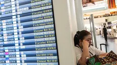 Seorang wanita beristirahat di samping papan informasi penerbangan di Terminal Internasional Bandara Haneda setelah penerbangan dibatalkan atau ditunda karena badai tropis Jangmi di Tokyo, Jepang, Rabu 3 Juni 2026. (Andrew CAALLERO-REYNOLDS/AFP)