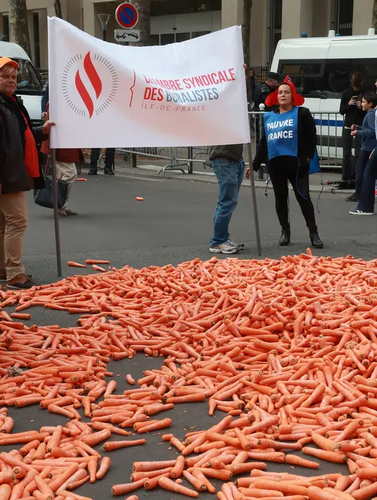 Penjual tembakau membentangkan spanduk di depan tumpukan wortel saat aksi protes di Paris, Rabu (4/10). Pada abad 15, tembakau dijual dalam bentuk gulungan daun yang diparut ujungnya sehingga menyerupai wortel. (AFP PHOTO/JACQUES DEMARTHON)