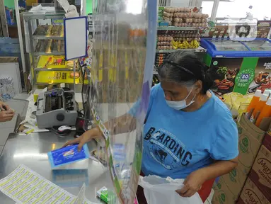 Pekerja melayani pembeli dari balik plastik pembatas pada sebuah minimarket di kawasan Cinere, Depok, Jawa Barat, Rabu (8/4/2020). Penggunaan plastik pembatas tersebut bertujuan untuk mengantisipasi penyebaran virus corona atau COVID-19 sebagai bentuk social distancing. (merdeka.com/Arie Basuki)