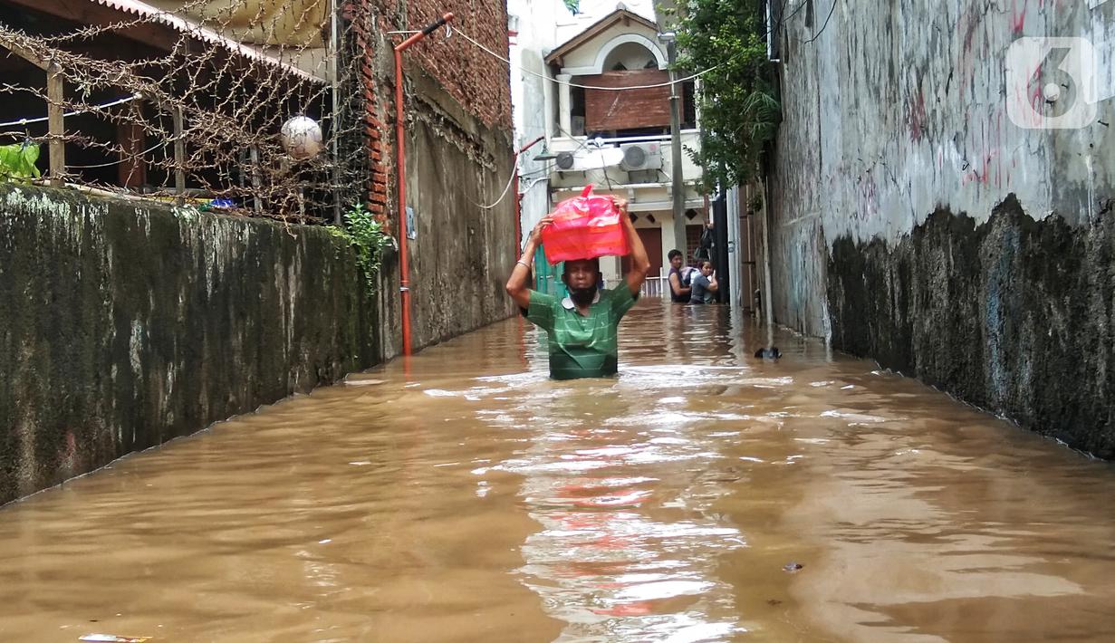 Warga berjalan menyusuri banjir yang merendam permukiman di kawasan Kebalen, Jakarta, Sabtu (20/2/2021). Curah hujan yang tinggi menyebabkan banjir setinggi orang dewasa di kawasan Kebalen. (Liputan6.com/Johan Tallo)