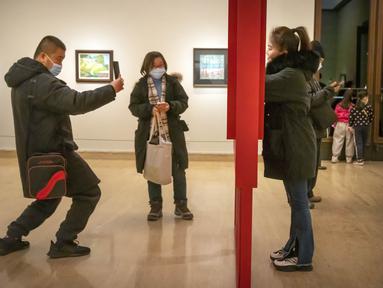 Seorang perempuan berpose untuk foto di galeri di Museum Seni Nasional China di Beijing, Rabu (1/2/2023). Pengunjung terus berduyun-duyun ke museum, situs bersejarah, dan tempat wisata di ibu kota China saat periode liburan Tahun Baru Imlek berakhir. (AP Photo/Mark Schiefelbein)