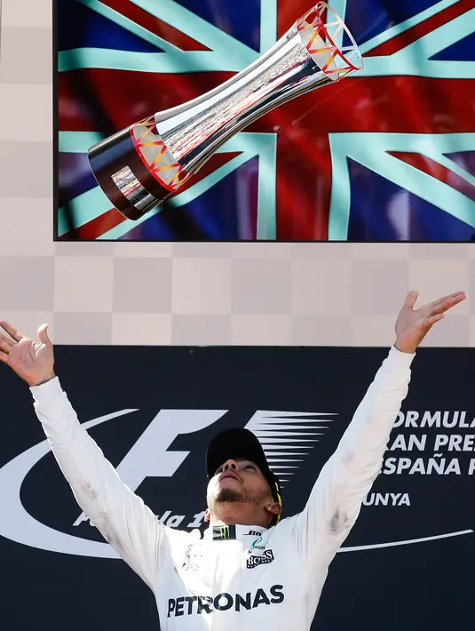 Pembalap Mercedes, Lewis Hamilton melemparkan trofi setelah memenangi balapan F1 GP Spanyol di Sirkuit Catalunya, Minggu (14/5). Meskipun memenangi GP Spanyol, Hamilton belum mampu merebut pimpinan klasemen dari Sebastian Vettel. (AP Photo/Manu Fernandez)