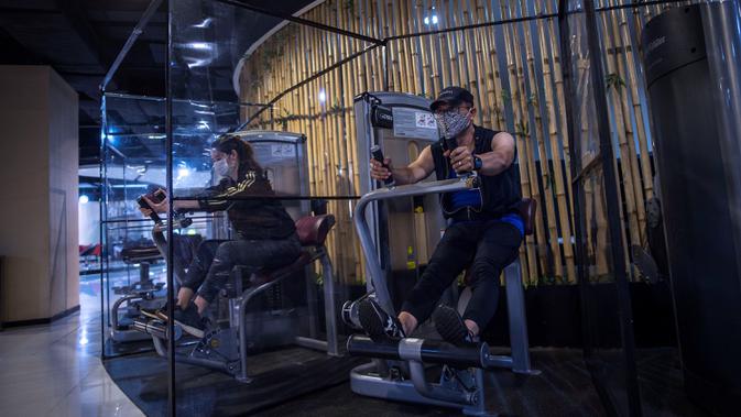 Orang-orang berolahraga dengan plastik penyekat untuk membatasi jarak antar pengunjung di sebuah tempat gym di Surabaya, Rabu (21/10/2020). Pusat kebugaran itu dibuka dengan menerapkan protokol kesehatan sebagai pencegahan COVID-19. (Juni Kriswanto / AFP)