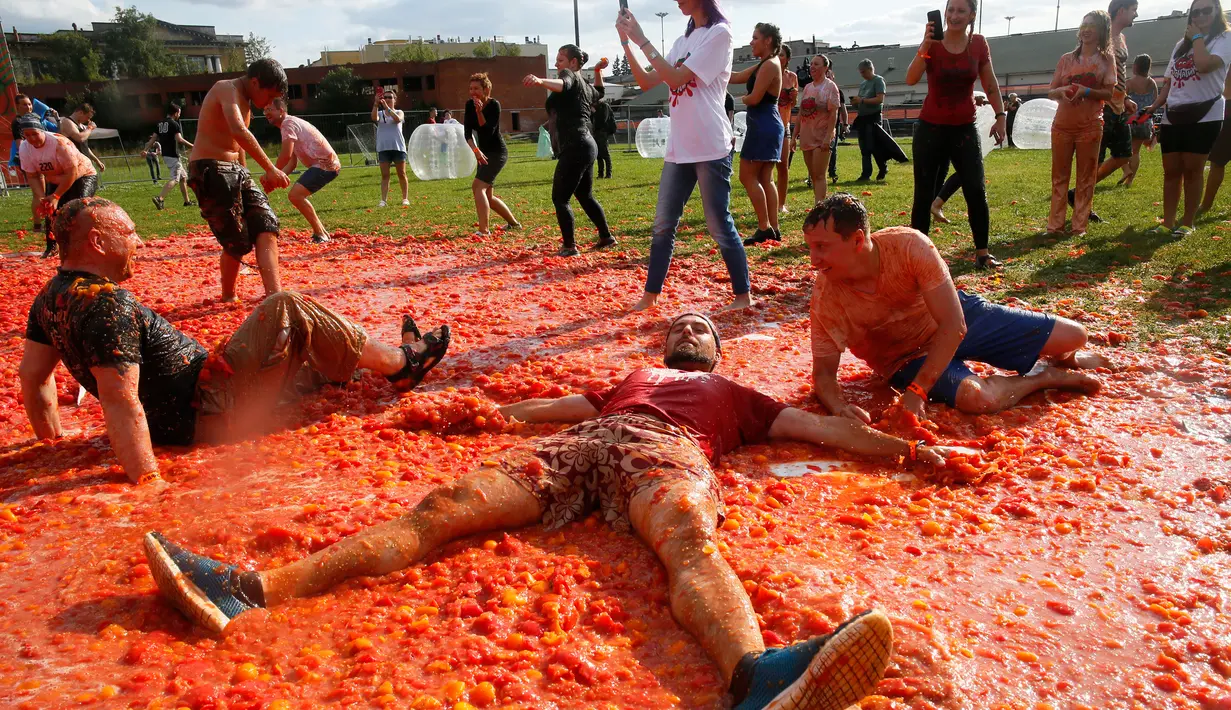 Peserta berbaring di atas tomat yang hancur ketika berpartisipasi dalam festival 'Tomatina' di St.Petersburg, Rusia, Minggu (18/8/2019). Tomatina atau perang tomat adalah festival Spanyol, dan tahun ini merupakan pertama kalinya dirayakan di Rusia. (AP Photo/Dmitri Lovetsky)