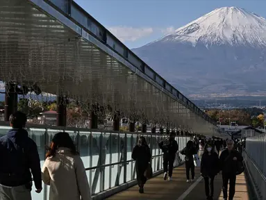 Foto yang diambil pada tanggal 28 November 2024 ini menunjukkan orang-orang berjalan di sepanjang jembatan yang menghubungkan toko-toko di pusat perbelanjaan populer dengan latar belakang Gunung Fuji di kota Gotemba, prefektur Shizuoka, sekitar 100 km di sebelah barat daya Tokyo. (Richard A. Brooks/AFP)