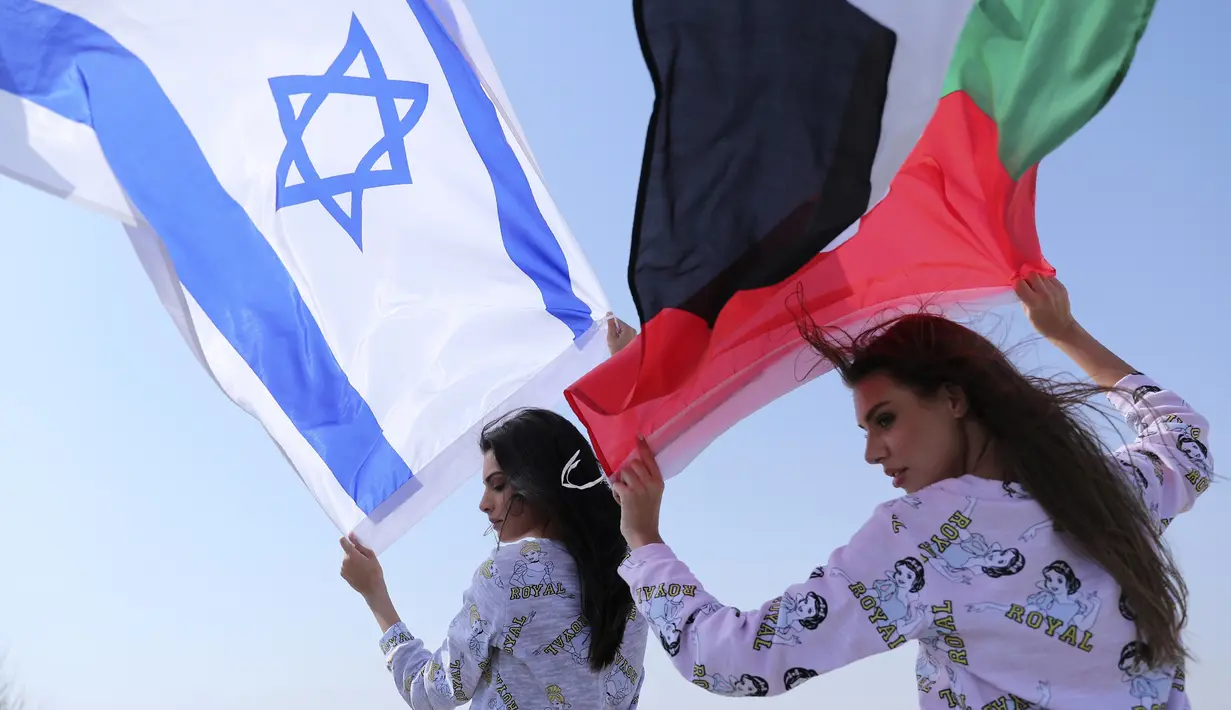 Model Israel May Tager (kiri) mengibarkan bendera Israel dan model Dubai asal Rusia Anastasia Bandarenka mengibarkan bendera Uni Emirat Arab saat pemotretan di Dubai, Uni Emirat Arab, 8 September 2020. Fix, merek pakaian dalam dan piyama Israel melakukan pemotretan di UEA. (AP Photo/Kamran Jebreili)