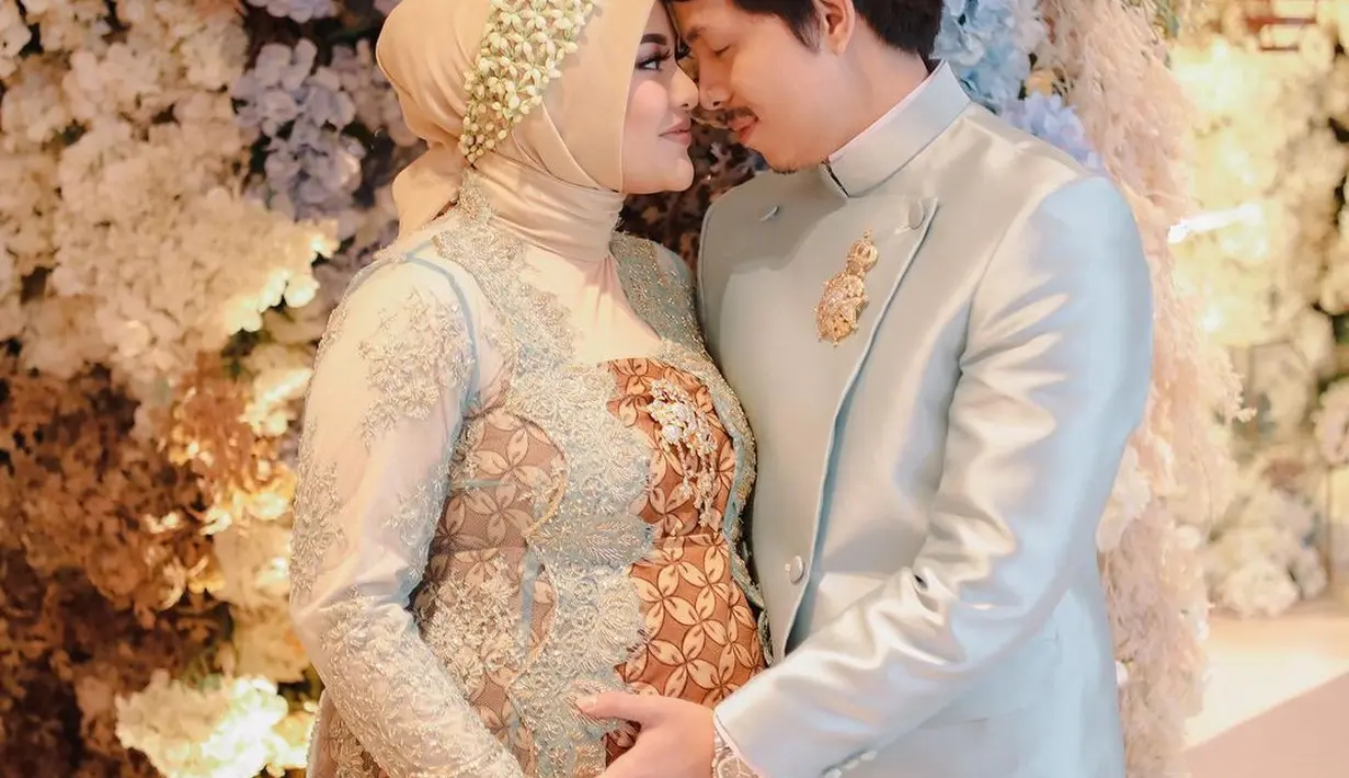Di acara Siraman pada upacara Mitoni baby Ameena, baik Aurel dan Atta memilih nuansa biru muda yang lembut. Aurel tampil elegan dengan kebaya transparan yang dipadunya dengan inner batik cokelat untuk siraman, serasi dengan beskap biru muda yang menawan dikenakan Atta. [Foto: Instagram/aurelie.hermansyah]