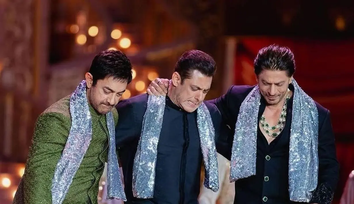 Potret trio menawan sedang berjoget di acara pre-wedding Anant Ambani. Shah Rukh Khan bersama Salman Khan dan Aamir Khan tampil di atas panggung mengenakan baju khas India. Salman memilih warna biru navy, sedangkan Aamir memilih Lungi berwarna hijau yang berkilauan. Ketiganya mengalungkan selendang berpayet biru muda yang berkilauan di bahu mereka. [Foto: Instagram/asianweddingmag]