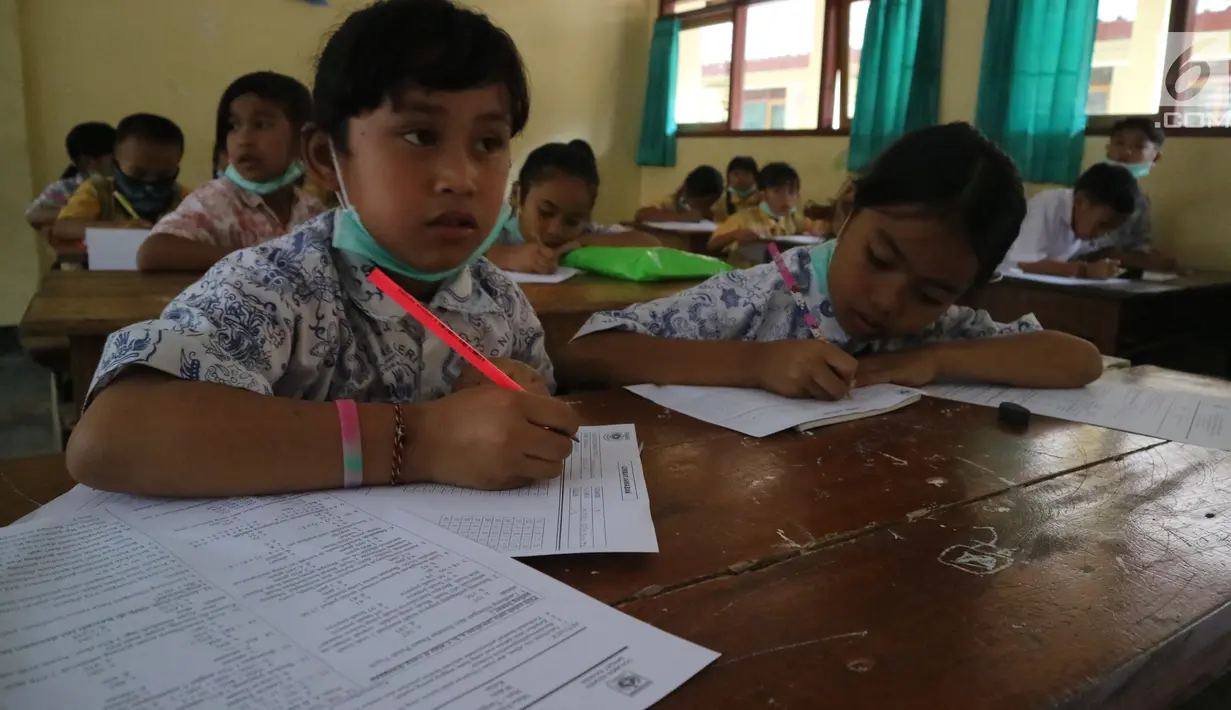 Para siswa mengerjakan soal UAS di SD Negeri 4 Rendang, Karangasem, Bali, Rabu (29/11). Kegiatan di beberapa sekolah yang masuk dalam kawasan KRB Gunung Agung masih terlihat meski beberapa wilayah mengalami hujan abu. (Liputan6.com/Andi Jatmiko)
