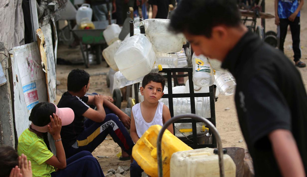 Warga Palestina yang mengungsi mengumpulkan air minum untuk dibawa kembali ke tempat penampungan mereka setelah rumah mereka hancur akibat bombardir Israel, di kamp pengungsi Bureij, Jalur Gaza Tengah pada Senin 18 Mei 2026. (Eyad Baba/AFP)