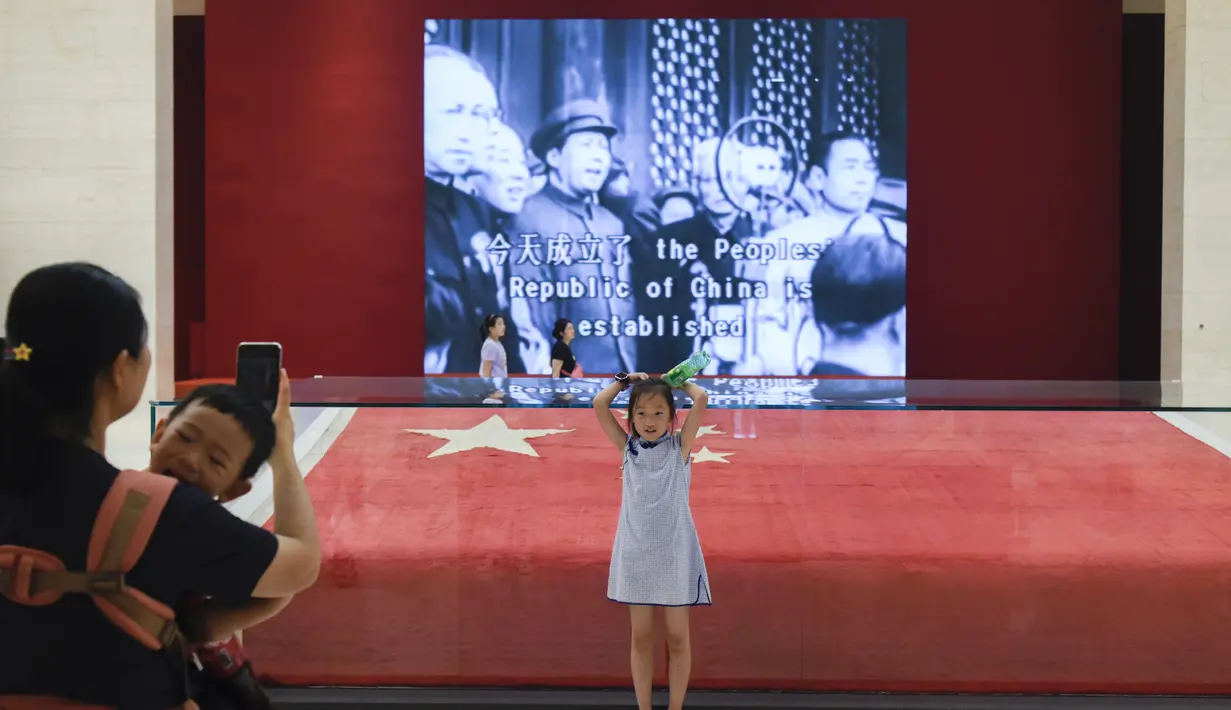 Seorang gadis berpose di depan bendera nasional Tiongkok yang dikibarkan pada 1 Oktober 1949 di Museum Nasional China di Beijing (22/8/2019). Museum Nasional Tiongkok memiliki empat lantai berisi aneka dokumen sejarah peradaban dan kisah perjuangan politik Tiongkok. (AFP Photo/Wang Zhao)