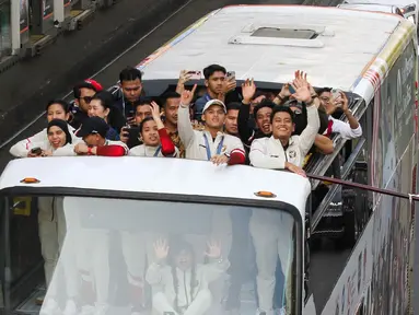 Para atlet Indonesia yang berlaga di Olimpiade Paris 2024 mengibarkan bendera Merah Putih saat berada di atas bus yang melintas dalam pawai di kawasan Bundaran HI, Jakarta, Kamis (15/8/2025). (Liputan6.com/Herman Zakharia)