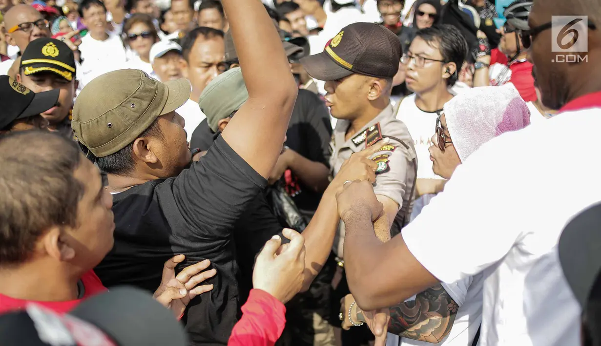 Seorang aparat kepolisian berusaha memisahkan massa berkaus #2019GantiPresiden dan #DiaSibukKerja yang saling sindir saat bertemu pada kegiatan Car Free Day di sisi barat Bundaran HI, Jakarta, Minggu (29/4). (Liputan6.com/Faizal Fanani)