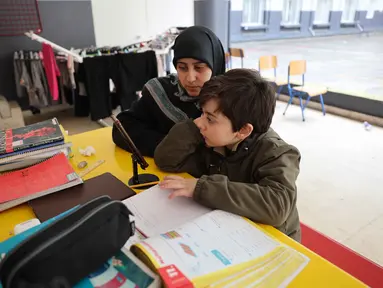 Seorang wanita Lebanon yang mengungsi duduk di samping seorang anak, mengawasi pelajaran daringnya melalui telepon seluler, di sebuah sekolah negeri yang diubah menjadi tempat penampungan di kota Dekwaneh, utara Beirut, pada Rabu 25 Maret 2026. Ketegangan di Lebanon semakin meningkat akibat eskalasi serangan udara yang dilakukan militer Israel. (Anwar AMRO/AFP)