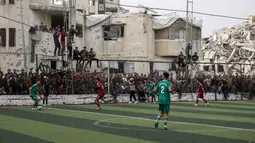 Seketika, aura kehidupan kembali bergelora melupakan luka perang yang masih terasa. Tampak dalam foto, warga Palestina menyaksikan pertandingan sepak bola lima lawan lima di tengah reruntuhan bangunan yang hancur di Kota Gaza pada Senin 9 Februari 2026. (Omar AL-QATTAA/AFP)