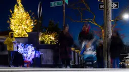 Wisatawan lewat saat seorang anak laki-laki menjual balon yang menyala di luar rumah yang dihiasi lampu Natal di lingkungan Dyker Heights, Brooklyn, New York, Amerika Serikat, 21 Desember 2022. Kawasan Dyker Heights menyajikan beberapa pameran akhir tahun yang paling mewah. (AP Photo/Julia Nikhinson)