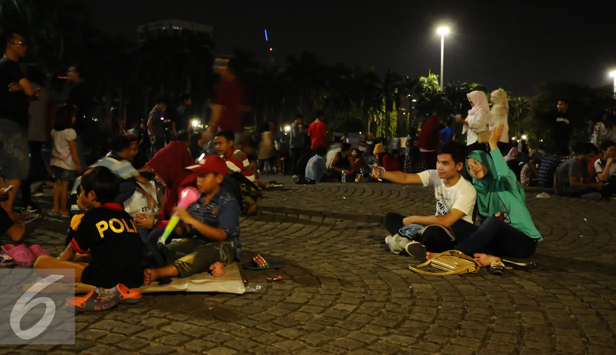Pengunjung duduk duduk di halaman Monumen Nasional, Jakarta, Sabtu (31/12). Dengan alasan keamanan, Pemprov DKI Jakarta membatalkan panggung hiburan malam pergantian tahun di kawasan Monumen Nasional. (Liputan6.com/Helmi Fithriansyah)