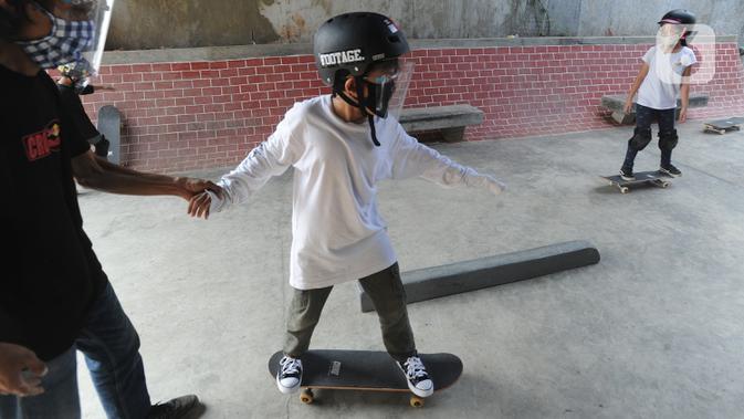 Instruktur melatih seorang anak menggunakan skateboard dengan memakai masker dan face shield di Crooz Shophouse di kawasan Duren Tiga, Jakarta Selatan, Minggu (2/8/2020). Mereka kembali melakukan latihan seminggu dua kali dengan menerapkan protokol kesehatan. (merdeka.com/Arie Basuki)