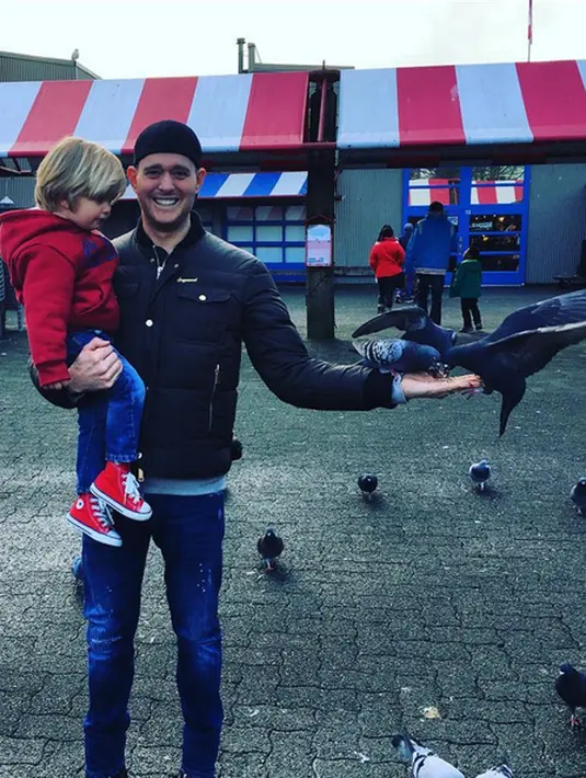 Noah, terlihat semakin mungil dan tampan dengan jaket dan sepatu merahnya. Ia tampak kagum melihat tiga ekor burung yang sedang makan di telapak tangan ayahnya. (Instagram/michaelbuble)
