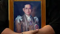 Seorang warga memegang foto Raja Bhumibol Adulyadej jelang pemindahan jenazah ke Grand Palace, Bangkok, Thailand, Jumat (14/10). (REUTERS / Athit Perawongmetha)