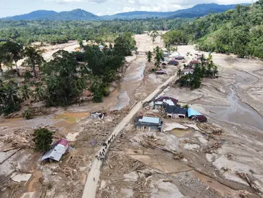 Warga berjalan di sepanjang jalan di sebuah desa yang terdampak banjir bandang di Batang Toru, Sumatera Utara, Senin 1 Desember 2025. Serangkaian bencana hidrometeorologi, yang mencakup banjir bandang (flash floods) dan tanah longsor dalam skala masif, menghantam beberapa wilayah di tiga provinsi di pulau Sumatera. (AP Photo/Binsar Bakkara)