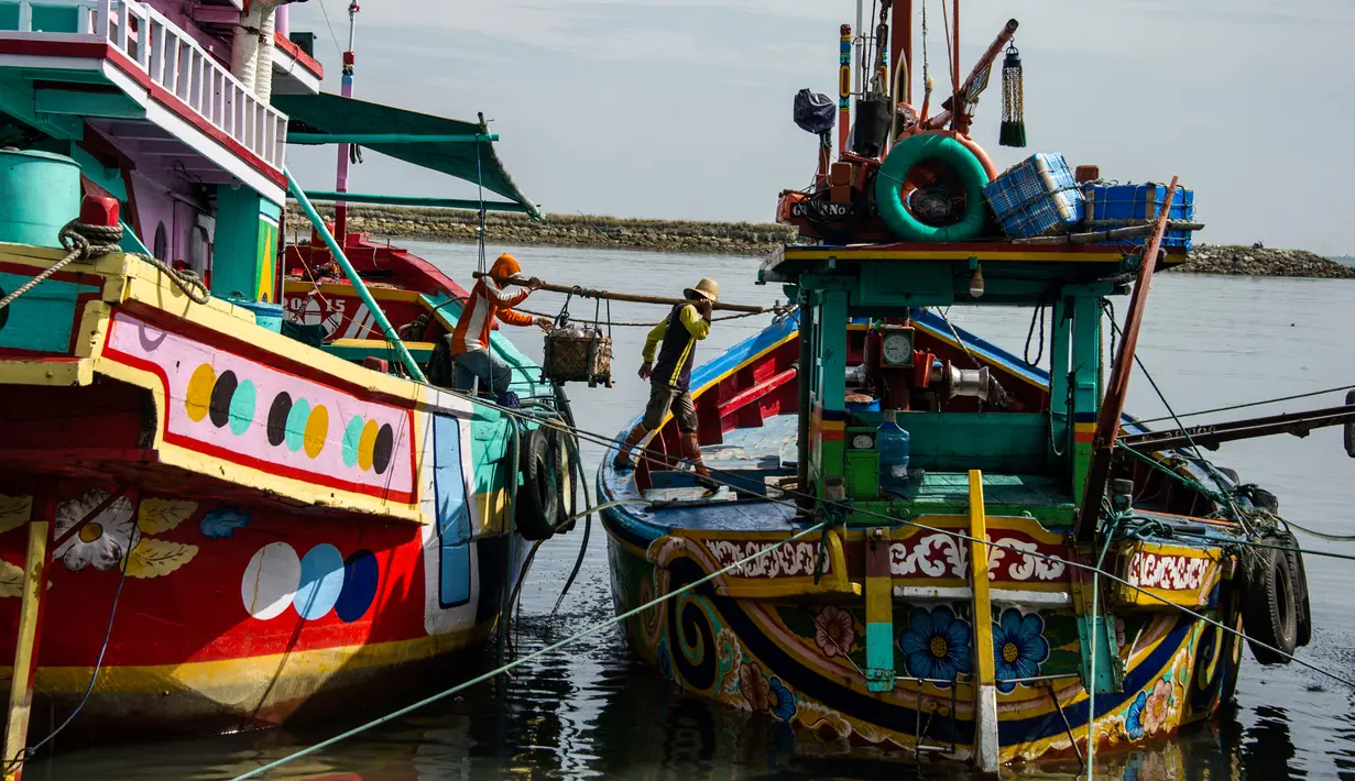 Dua nelayan membawa hasil tangkapannya dari perahu saat tiba di sebuah tempat pelelangan ikan di Brondong, Lamongan, Jawa Timur, Senin (13/3). (AFP Photo/Juni Kriswanto)