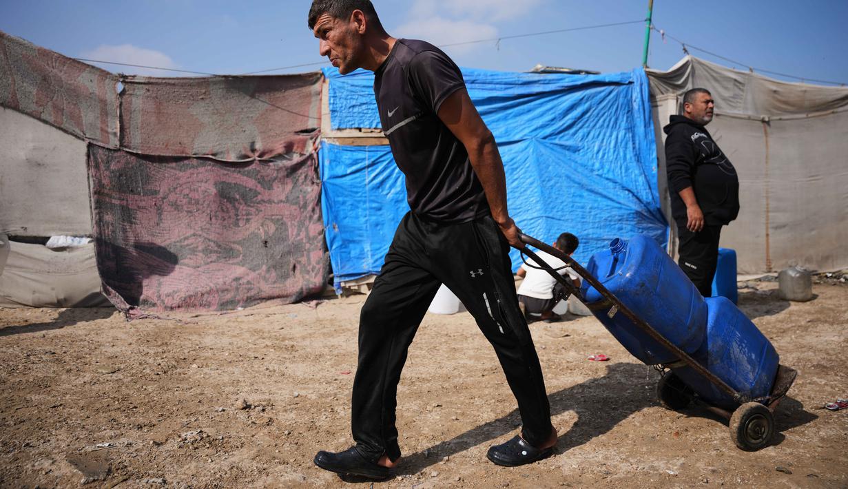 Sebagai informasi, sekitar 90 persen fasilitas air, sanitasi, sumur, dan jaringan pipa di Gaza rusak atau hancur akibat serangan Israel sejak Oktober 2023 silam. Tampak dalam foto, seorang pria Palestina membawa jerigen berisi air melalui perkemahan tenda di Khan Younis, Jalur Gaza Selatan, Kamis 30 April 2026. (AP Photo/Abdel Kareem Hana)