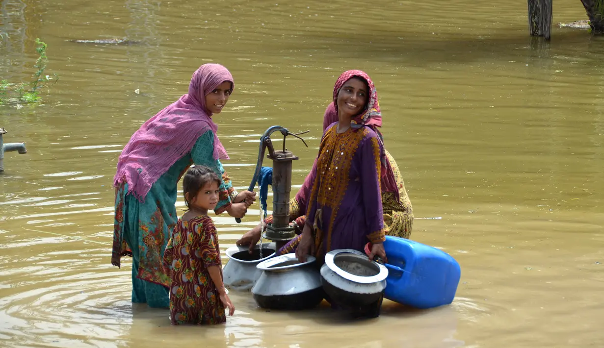 Wanita yang terkena banjir mengisi air minum dari pompa tangan di tengah jalan yang banjir setelah hujan lebat di distrik Jaffarabad di provinsi Balochistan (29/8/2022). Jumlah korban tewas akibat banjir monsun di Pakistan sejak Juni telah mencapai 1.136, menurut angka yang dirilis pada 29 Agustus oleh Otoritas Manajemen Bencana Nasional negara itu. (AFP/Fida Hussain)