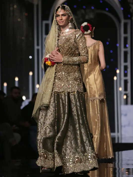 Seorang model mengenakan busana rancangan desainer Faike Karim selama Bridal Couture Week di Lahore, Minggu (9/12). Kreasi gaun pengantin yang ditampilkan didominasi kain sari yang menjadi ciri khas wanita Pakistan. (AP Photo/K.M. Chaudary)